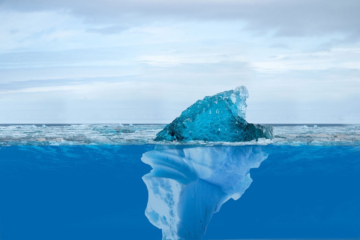 Iceberg on blue water. The tip is showing above the water with the majority of the iceberg below the surface.